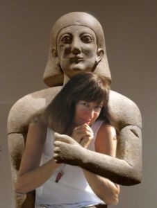 Robin Botie being hugged at the Metropolitan Museum of Art by a statue from Mesopotamia or Sumeria or -